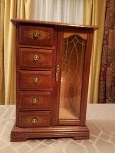 an antique wooden jewelry cabinet with glass doors and drawers in the middle, on a bed