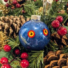 a blue ornament sitting on top of pine cones next to red berries and pine cones