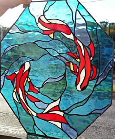 a stained glass window with red and white fish swimming in the water, on top of a wooden table