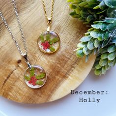 two necklaces sitting on top of a wooden plate next to a plant and pine cone