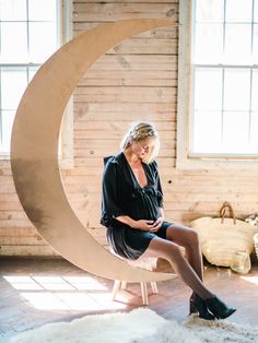 a woman sitting on top of a chair in front of a crescent shaped sculpture with her legs crossed