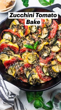 an iron skillet filled with cooked zucchini and tomato slices on a white table