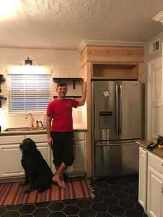 a man standing next to a black dog in a kitchen