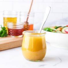 a glass jar filled with liquid sitting on top of a counter next to a bowl of salad