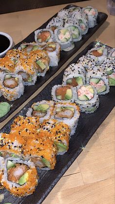 sushi is served on black plates with dipping sauce