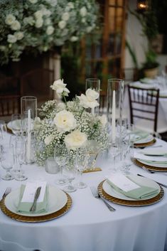 the table is set with white flowers and place settings