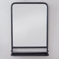 a black metal frame mirror hanging on the wall with a shelf underneath it that has a white blank space for text