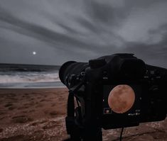 a camera on a tripod with the moon in the sky and beach behind it