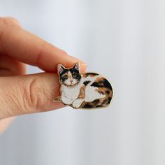 a cat pin sitting on top of someone's finger