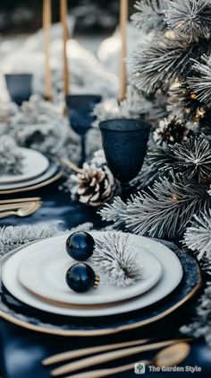 the table is set with black and white plates, silverware, pine cones, and candlesticks