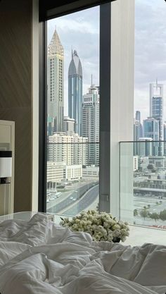 a bed sitting in front of a large window next to a tall cityscape