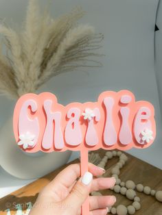 a hand holding a pink cake topper with the word charlie spelled in large letters