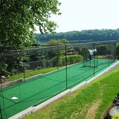 an outdoor tennis court surrounded by lush green grass and trees, with a man on the far side