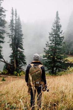 a man with a backpack is walking through the foggy woods on a trail in the mountains