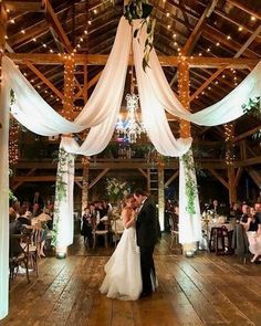 a bride and groom kissing in front of an open air venue with white draping