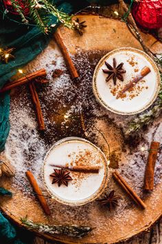 two mugs filled with cinnamon and spices on top of a wooden board next to christmas decorations