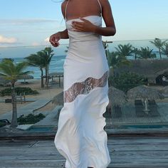 a woman in a white dress standing on a wooden deck next to the ocean and palm trees