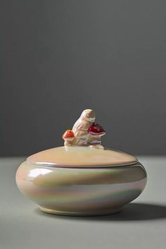 a ceramic bowl with a small figurine sitting on it's top, in front of a gray background