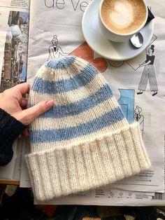 a person holding a knitted hat next to a cup of cappuccino