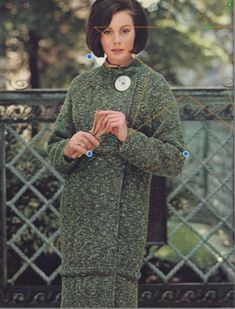 a woman in a green coat and hat standing next to a fence with her hands on her hips