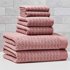 six pink towels stacked on top of each other in front of a white brick wall