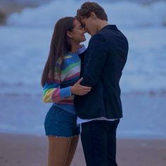 a man and woman standing next to each other on the beach with waves in the background