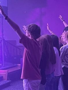 a group of people standing next to each other in front of a purple wall holding their hands up