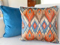 two blue and orange pillows sitting on top of a white couch next to each other