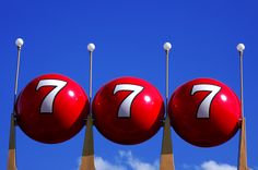 three red balls with the number seven on them are in front of a blue sky