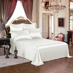 a bed with white sheets and pillows in a bedroom next to a chandelier