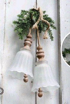 two white glass bell lights hanging from a wooden wall with pine cones and twine