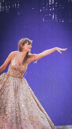 a woman in a gold dress on stage with her arms out and one hand outstretched