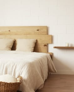 a bed with white sheets and pillows next to a basket on the floor in front of it