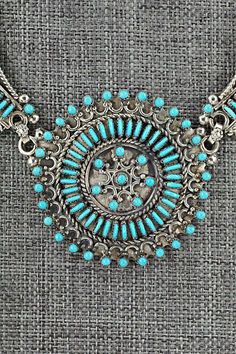 This beautiful turquoise and sterling silver necklace and earrings set was made by Zuni silversmith Connie Wyaco. The back of the pendant is signed.Necklace: 14"Pendant Length: 1 1/2"Pendant Width: 1 1/2"Station Length: 1 1/2"Station Width: 3/4"Earrings:Length: 1 1/2"Width: 1/4"Free shipping on all orders! We ship with USPS and always include tracking. All orders ship within a day of payment.Returns are accepted up to 30 days after you receive your order. Just send us a message. Our shop offers Turquoise Jewelry With Intricate Design, Traditional Silver Turquoise Necklace With Large Pendant, Traditional Turquoise Necklace With Large Sterling Silver Pendant, Traditional Turquoise Sterling Silver Necklace, Traditional Turquoise Jewelry Stamped 925, Traditional Turquoise Medallion Jewelry, Turquoise Sterling Silver Necklace For Wedding, 4 Earrings, Silver Necklace Set