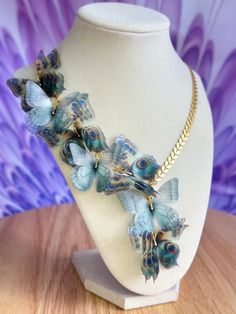 a necklace with blue and green butterflies on it sitting on a white mannequin