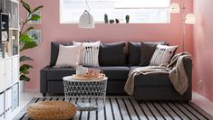 a living room with pink walls and black couch in the corner, coffee table on top of it