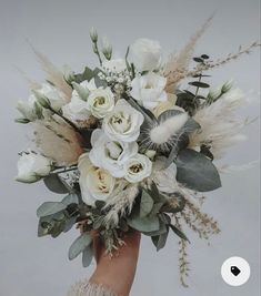 a hand holding a bouquet of white flowers and greenery