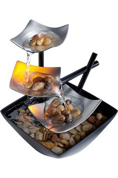 three metal trays with food and water pouring from them to each other on top of rocks