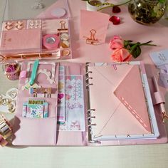 an open pink planner book sitting on top of a table next to flowers and other items