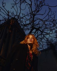 a woman standing in front of a tree at night with her eyes closed and head turned to the side