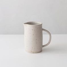 a white coffee mug with speckles on it sitting on a table next to a wall