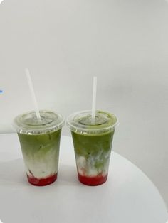 two drinks with straws sitting on top of a white table next to each other