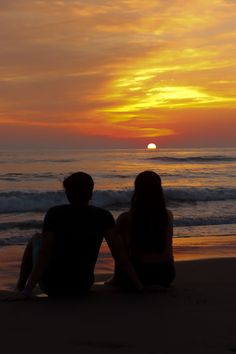 two people sitting on the beach watching the sunset