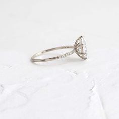 a white gold ring with a pear shaped diamond set in the center, on a white background