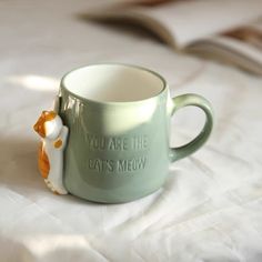 a coffee cup with a cat's meow on it sitting on a bed