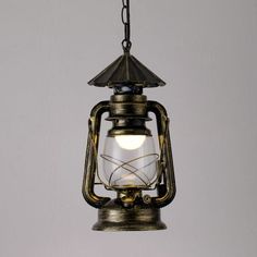 an old fashioned lantern hanging from a chain on a gray wall with the light turned on