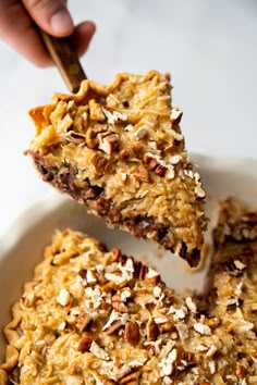 a person holding a spoon over a bowl filled with granola and oatmeal bars