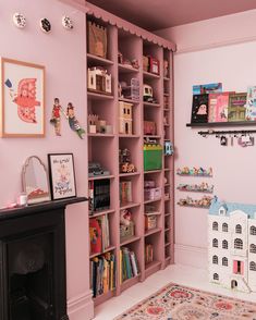 a pink room with bookshelves and toys on the shelves in front of a fireplace