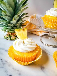 pineapple cupcakes with white frosting and fresh pineapple on the side