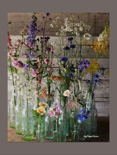 a bunch of glass vases with flowers in them on a wooden table next to a wall